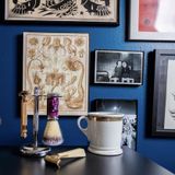 Vintage shaving tools sit on a table in front of a blue wall with pictures hanging