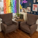 The interior of the shop facing the doo, two brown chairs face eachother and a rainbow flag hangs in the window